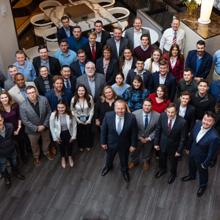 Large group photo of Leadership Institute staff, interns, and program participants gathered in the lobby of LI headquarters. The diverse group of conservative activists and students pose together in business and business casual attire on the modern tiled floor.