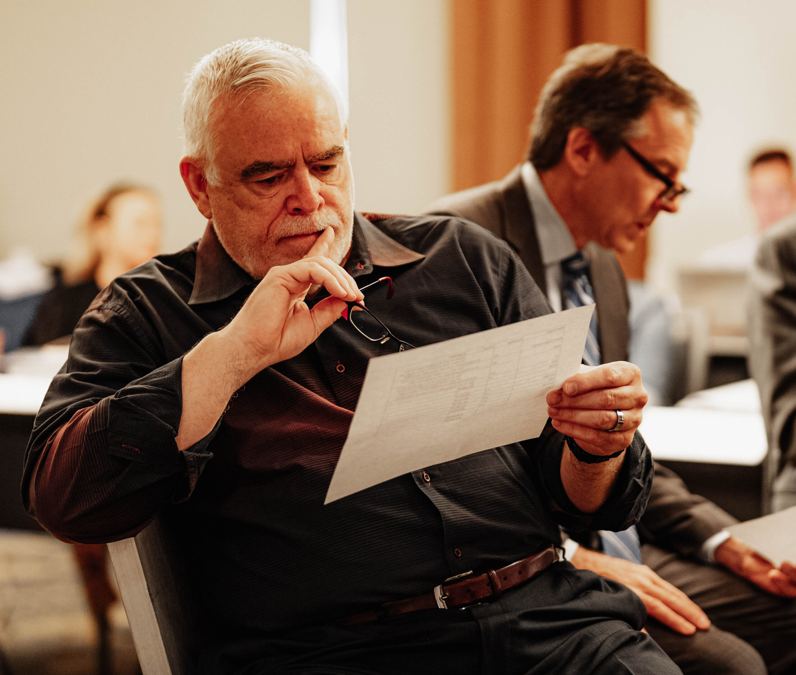 A man with gray hair and mustache reads training materials while holding his glasses during a Leadership Institute workshop session.